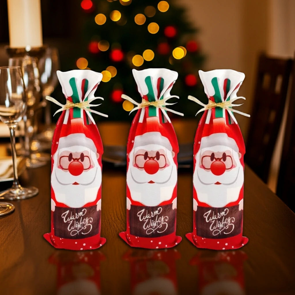 Drei Stoff-Flaschenhüllen mit klassischem Weihnachtsmann-Motiv, auf dunklem Holztisch mit verschwommenem Weihnachtsbaum im Hintergrund.